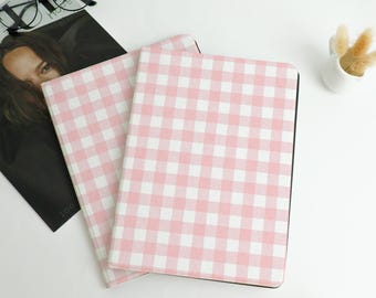 Può includere: Due quaderni con copertine a motivo a quadri rosa e bianchi. I quaderni sono impilati, con quello superiore leggermente angolato. Una rivista e occhiali sono sullo sfondo.