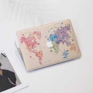 May include: A beige laptop skin with a colorful world map design. The map features various landmarks and icons, including airplanes, buildings, and animals. The text "WORLD MAP" is written in a banner at the bottom of the map.