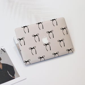 May include: A light grey laptop computer with a black bow pattern on the lid. The Apple logo is visible on the lid.