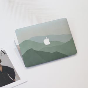 May include: A laptop featuring a green and grey mountain range design. The laptop has a white Apple logo. The design incorporates layers of green and grey hues, creating a landscape effect.