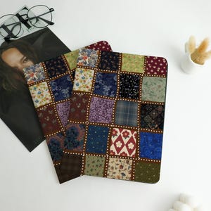 May include: Two notebooks with a patchwork design featuring squares of various floral and patterned fabrics in shades of blue, green, red, and brown. The notebooks are on a white surface with a magazine and glasses.