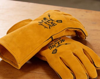 May include: A pair of yellow grilling gloves with black trim. The gloves have the words "KING OF THE GRILL" and a graphic of a spatula and grill printed on them. The name "George" is printed below the text.
