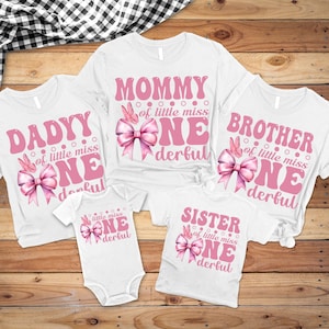 May include: White t-shirts and a onesie with pink text and graphics. The shirts read "Mommy," "Dadyy," "Brother," and "Sister" with "One" and "Wonderful" in a retro font. A pink bow and butterfly graphic is included.