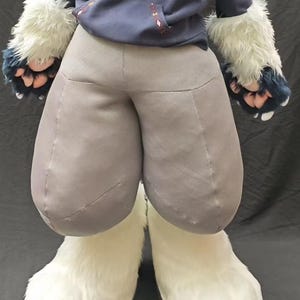 May include: A costume featuring a dark blue hooded sweatshirt with a geometric pattern, grey padded trousers, and white faux fur leg coverings. The costume includes matching white and dark blue faux fur hand coverings with visible paw pads.