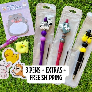Peut inclure: Ensemble de papeterie comprenant trois stylos décoratifs avec des figurines d'animaux, des autocollants et un bloc-notes. Les stylos présentent des motifs de zèbre, de chat et d'abeille. Le bloc-notes porte la mention "ANIMAL PARADISE".