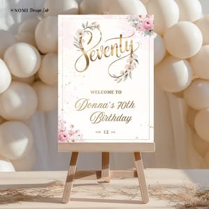 May include: A wooden easel supports a sign for Donna's 70th birthday. The sign has gold script reading "Seventy" and "Welcome to Donna's 70th Birthday." Floral accents and a pink background are also present in the design.