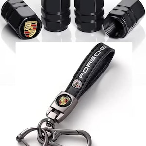 May include: Black tire valve stem caps featuring the Porsche logo, alongside a black leather keychain with "PORSCHE" and the Porsche emblem. The keychain includes a silver-coloured clasp.