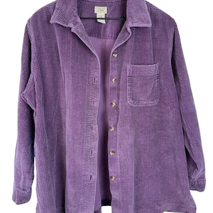 May include: A long-sleeved purple corduroy shirt featuring a classic collar, a front button-down closure with light-colored buttons, and a single chest pocket on the left side. The interior neck label displays the L.L. Bean brand name.