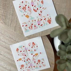 May include: Two white paper cutouts with the number "99" and the word "ice cream" in a playful font. The numbers and letters are decorated with a pattern of ice cream cones and cherries in pastel colors. The cutouts are on a wooden surface.