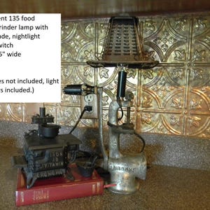 May include: A repurposed food chopper/grinder lamp with a toaster shade, nightlight, and inline switch. The lamp is 17 inches tall and 9.5 inches wide. The lamp is made of metal and has a silver finish. The lamp is sitting on a book with the words "Iron is Vitamin" printed on it. The lamp is plugged into an electrical outlet.