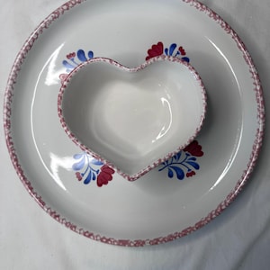 May include: White ceramic serving dish set. The set includes a large round plate and a heart-shaped bowl. Both pieces have a pink dotted border and are decorated with red and blue floral designs.