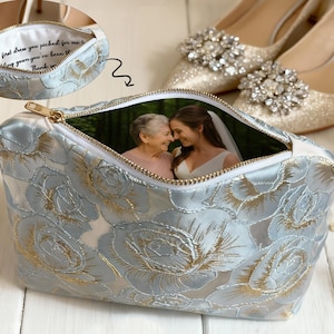 May include: A light blue floral print cosmetic bag with a gold zipper, featuring a photo of two women inside. The bag is next to a pair of sparkly gold heels and a lit candle.