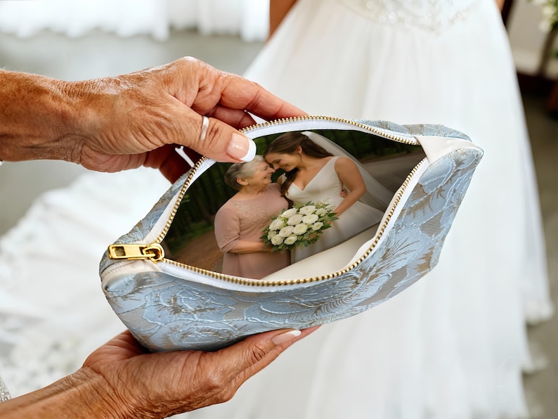 May include: A light blue floral patterned pouch with a gold zipper, holding a photograph of a bride and another woman. The pouch is held by a person with aged hands, and the background shows a white wedding dress.