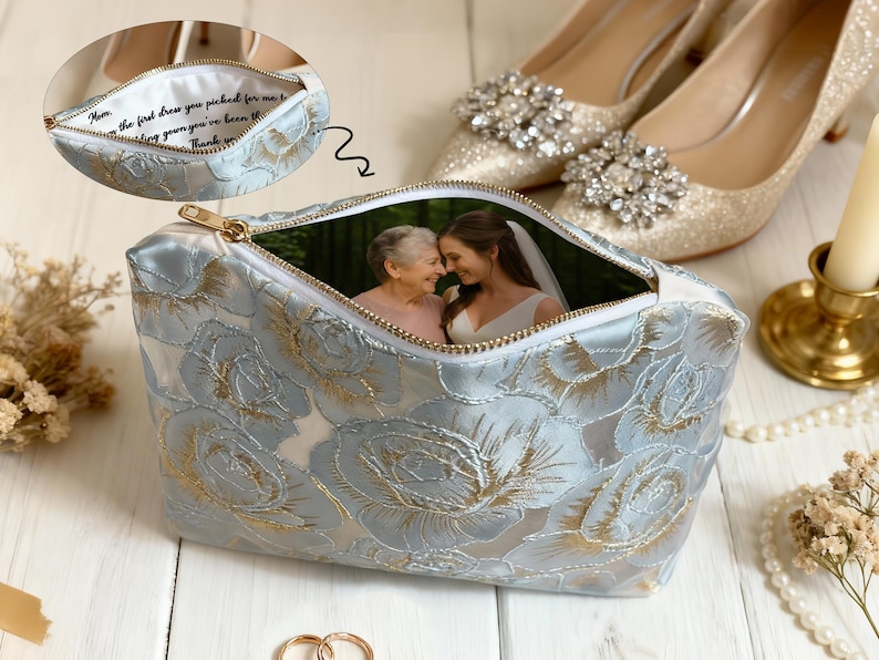 May include: A light blue floral print cosmetic bag with a gold zipper, featuring a photo of two women inside. The bag is next to a pair of sparkly gold heels and a lit candle.