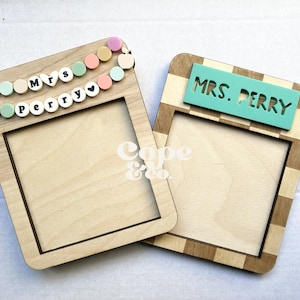 May include: Two wooden picture frames with blank spaces for photos. The frame on the left has a colorful garland with the text "Mrs. Perry" on it. The frame on the right has a checkered pattern and the text "MRS. PERRY" on it.