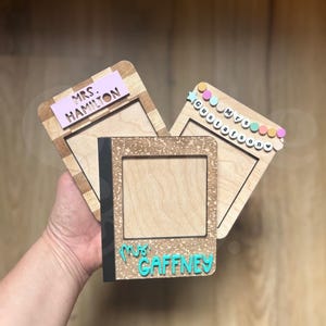 May include: Three wooden picture frames with teacher names. One frame has a pink rectangle with "MRS. HAMILTON" in white. Another has "Mrs. Gustafson" in colorful letters. The third frame is notebook-shaped with "Mrs. Gaffney" in teal.