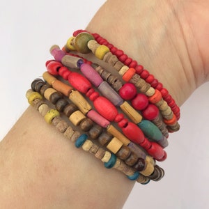 May include: A selection of vibrant wooden bead bracelets. The bracelets showcase a mix of shapes and colours, including red, yellow, orange, purple, and brown. The beads are strung on elastic cords.