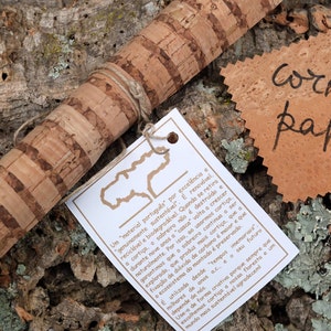Può includere: Un primo piano di un rotolo di carta di sughero con un'etichetta bianca che recita "Um "material português por excelência"..." e un piccolo pezzo di carta di sughero con la parola "cork paper" scritta su di esso.