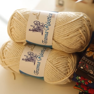 May include: Two balls of natural colored yarn with blue and white labels that read "Trama Rustica 500g".