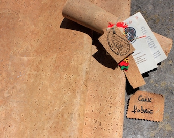 May include: A roll of cork fabric with a brown, speckled texture. The fabric is rolled up and tied with a colorful ribbon. A small tag with the text "Cork Fabric" is attached to the roll.