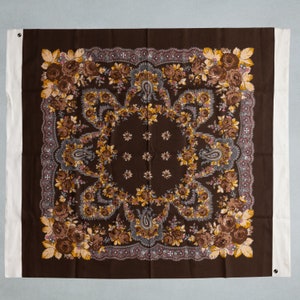 Può includere: Una sciarpa quadrata marrone con un motivo floreale. Il motivo presenta un disegno ripetitivo di fiori, forme paisley e piccole stelle. La sciarpa ha un bordo bianco.