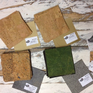 May include: Assortment of cork fabric samples in various colors and textures, including natural cork, green cork, and brown cork. The samples are labeled with "Backing" and the type of cork. There are also small cards with the word "FOLICLORE" printed on them.