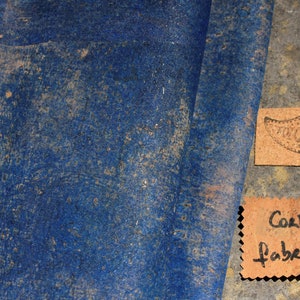 Può includere: Un primo piano di un tessuto di sughero blu con un'etichetta di sughero marrone che dice "Cork Fabric" e un'altra etichetta di sughero marrone con un motivo paisley e la parola "FIZZLEOREY".