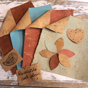 Può includere: Quattro pezzi di tessuto in sughero reversibile in vari colori, tra cui marrone, blu, rosso e verde. Il tessuto è testurizzato e ha un aspetto naturale di sughero. Il tessuto è disposto in una pila, con il pezzo superiore piegato per mostrare il retro. Il tessuto è etichettato "Tessuto in sughero reversibile".