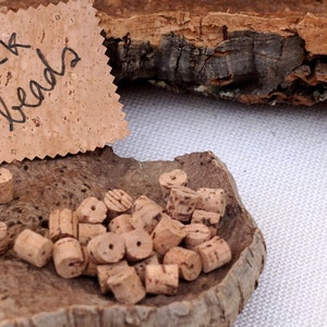 May include: A close-up of a pile of natural cork beads on a piece of cork bark. The beads are light brown and have a natural, rustic look. A sign made of cork reads "cork beads".