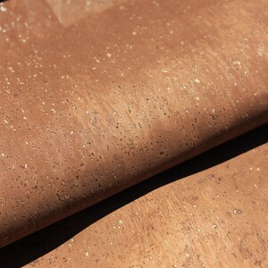 May include: Close-up of a brown cork sheet with a textured surface. The cork has a natural, speckled appearance with small, light-colored flecks throughout.