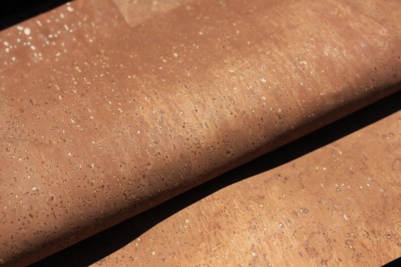 May include: Close-up of a brown cork sheet with a textured surface. The cork has a natural, speckled appearance with small, light-colored flecks throughout.