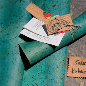 May include: A roll of teal cork fabric with a brown paper tag that says "Cork Fabric". The fabric is rolled up and tied with twine. There are other tags and papers on top of the fabric.