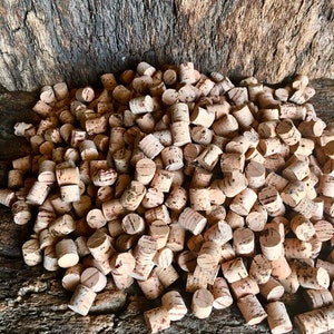 Könnte beinhalten: Ein großer Haufen natürlicher Korken für Flaschen. Die Korken sind hellbraun und haben eine leicht raue Textur. Sie sind in einem zufälligen Muster auf einer Holzoberfläche angeordnet.