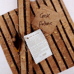 May include: Two rolls of cork fabric with black stripes. The fabric is natural and has a rustic look. The rolls are tied together with twine and a tag that reads "pele de corti&ccedil;a".