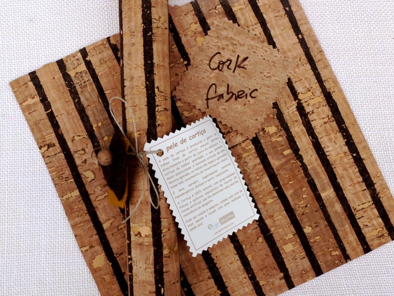 May include: Two rolls of cork fabric with black stripes. The fabric is natural and has a rustic look. The rolls are tied together with twine and a tag that reads "pele de corti&ccedil;a".
