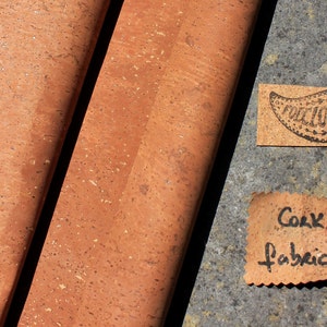 May include: Two rolls of cork fabric, one on top of the other, with a brown speckled pattern. The fabric is rolled up and the edges are visible. There are two small pieces of cork fabric with text on them. One says "Cork Fabric" and the other says "Follicle".
