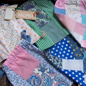 May include: A collection of five patchwork fabric bags with different patterns and colours. The bags are made of cotton fabric and have a variety of designs, including polka dots, stripes, and floral prints. The bags are all handmade and have a unique, vintage look. One bag has the word "NAOPICA" printed on it.