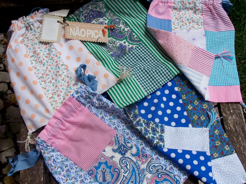 May include: A collection of five patchwork fabric bags with different patterns and colours. The bags are made of cotton fabric and have a variety of designs, including polka dots, stripes, and floral prints. The bags are all handmade and have a unique, vintage look. One bag has the word "NAOPICA" printed on it.