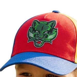 May include: A baseball cap with a red crown, blue peak, and yellow side panels. The cap displays a green and white stylized cat face logo. A bright and colourful accessory.