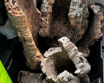 May include: A collection of natural cork bark pieces with rough, textured brown and grey surfaces. The pieces vary in shape, featuring hollow, tube-like structures and flat, curved segments with deep ridges and organic, uneven edges throughout.