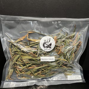May include: A clear plastic bag filled with dried green bamboo leaves. The bag has a white label with the text "Hypnotic Aquatics" and "Bamboo Leaves". The bottom of the bag has a smaller white label with the text "Hypnotic Aquatics, Living art made simple."