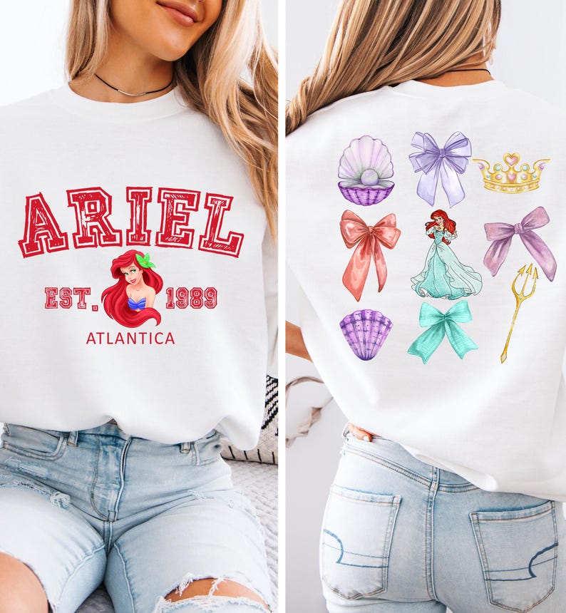 Disney Ariel sweatshirt in pastel blue with bold red varsity lettering on the front, reading 'Ariel Est. 1989 Atlantica.' The back design includes princess elements like seashells, bows, a golden trident, and an elegant illustration of