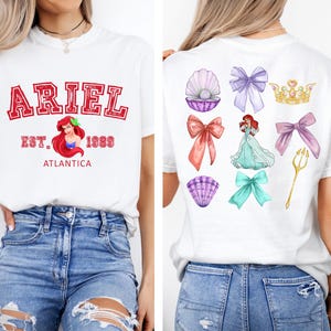 Disney Ariel sweatshirt in pastel blue with bold red varsity lettering on the front, reading 'Ariel Est. 1989 Atlantica.' The back design includes princess elements like seashells, bows, a golden trident, and an elegant illustration of
