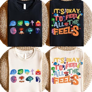 May include: Two t-shirts, one black and one cream, featuring the characters from the movie Inside Out. The black t-shirt has the characters in a row across the chest. The cream t-shirt has the characters in a circle around the text "It's okay to feel all the feels".