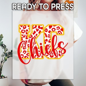 May include: A white graphic featuring the text "READY TO PRESS" at the top. Below, the letters "KC" are in a yellow outline with a red and white leopard print pattern. The word "Chiefs" is written in red script below the letters.