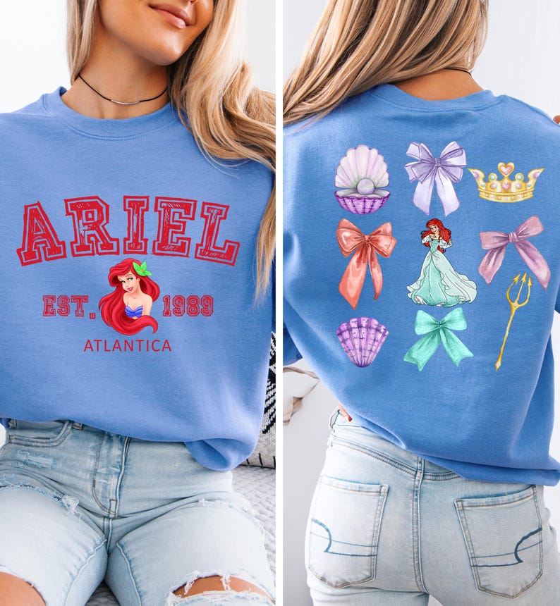 Disney Ariel sweatshirt in pastel blue with bold red varsity lettering on the front, reading 'Ariel Est. 1989 Atlantica.' The back design includes princess elements like seashells, bows, a golden trident, and an elegant illustration of