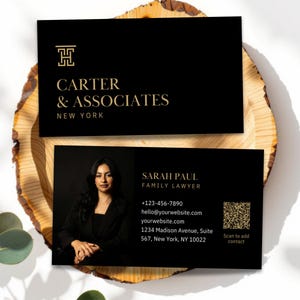 Peut inclure: Deux cartes de visite noires avec du texte doré et un portrait de femme, présentées sur une tranche de bois. La carte supérieure indique "CARTER & ASSOCIATES NEW YORK". La carte inférieure présente "SARAH PAUL FAMILY LAWYER" et les coordonnées.