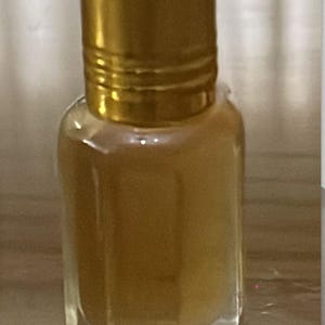 Pode incluir: Uma pequena garrafa de vidro transparente com uma tampa dourada. A garrafa cont&eacute;m um l&iacute;quido castanho claro. A tampa &eacute; cil&iacute;ndrica e tem um design canelado. A garrafa tem uma forma retangular com bordas chanfradas.