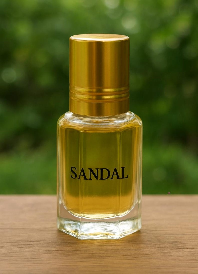 Pode incluir: Um frasco de perfume de vidro transparente com tampa dourada, preenchido com um l&iacute;quido &acirc;mbar claro. A palavra "SANDAL" est&aacute; impressa em preto na frente. O frasco est&aacute; sobre uma superf&iacute;cie de madeira.