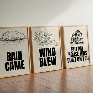 May include: Three framed prints with black and white illustrations and text. The first print shows a rain cloud with the text "Rain Came". The second print shows a swirling cloud with the text "Wind Blew". The third print shows a house with the text "But My House Was Built On You".